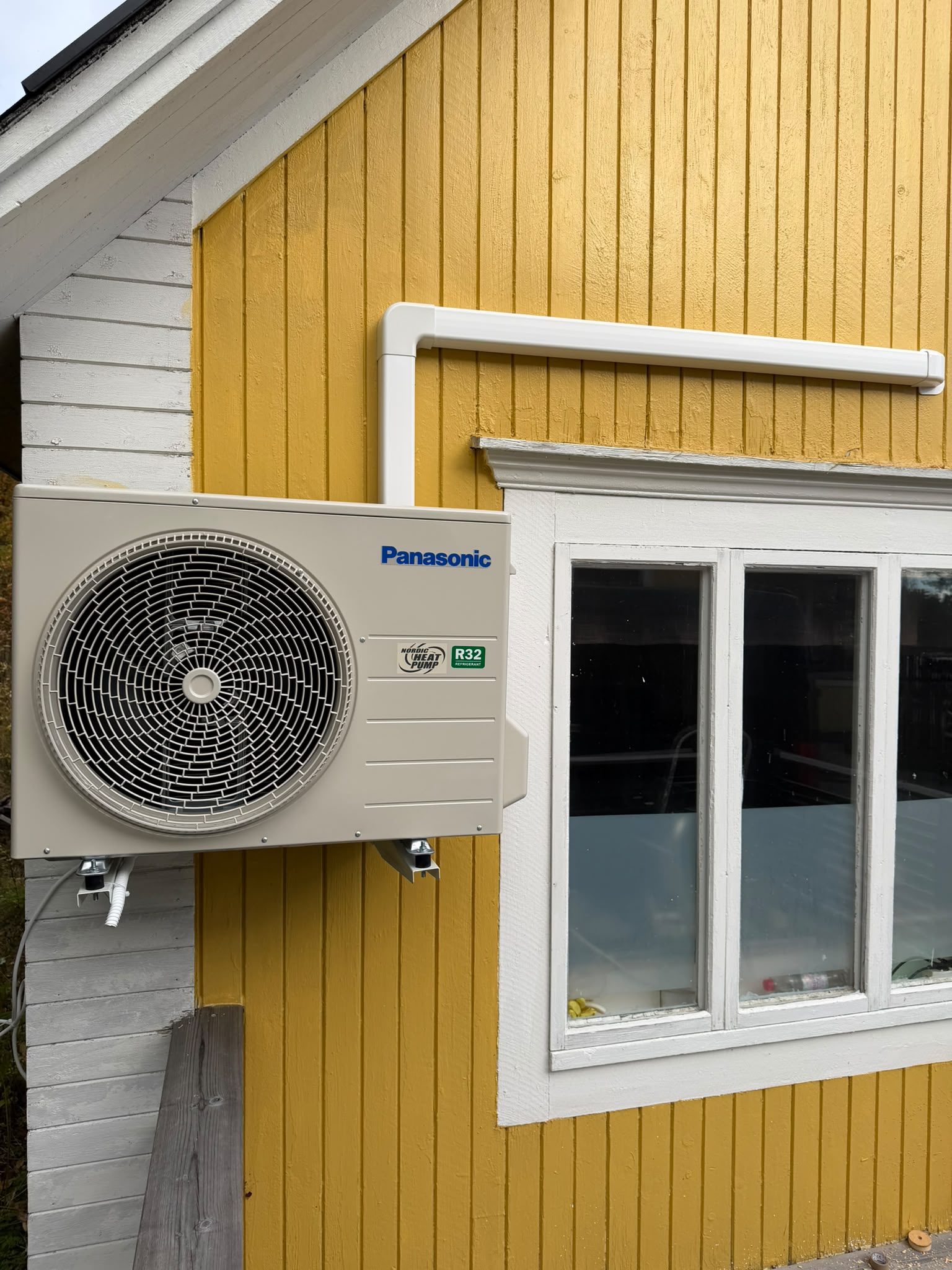 Panasonic Nordic Heat Pump utedel monterad på gul träfasad i Byske av MH Värmepumpar
