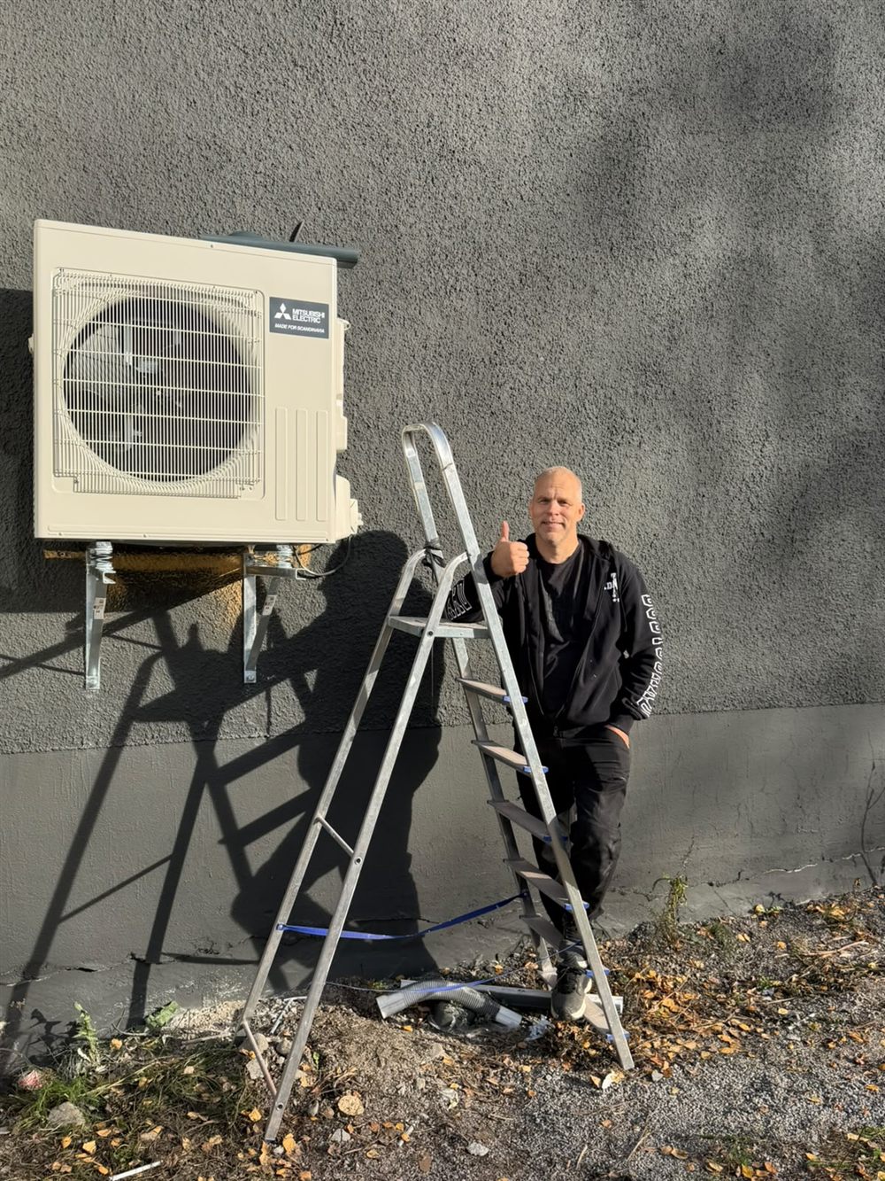 Mitsubishi Electric utedel monterad på grå putsfasad av MH Värmepumpar